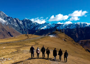 A group of people hiking across a grassy ridge toward mountains with snow-covered peaks.